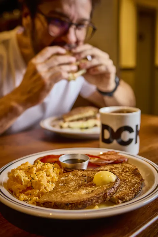 Prato de ovos, bacon e torrada ao lado da caneca com o nome DCK.