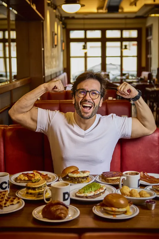 Cliente na cabine vermelha da DCK, com a mesa cheia de pratos de brunch.